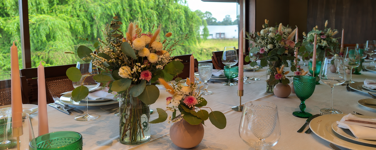 Composição floral com vários arranjos em tons creme, rosa e verde numa mesa de evento decorada pela Paula Florista