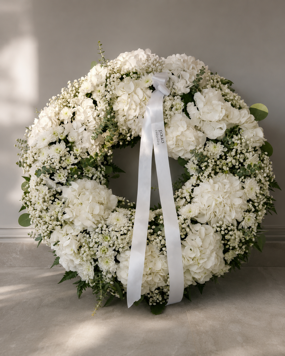 Coroa floral branca de homenagem com hortênsias, gipsofila e folhagem preparada pela Paula Florista em Fafe