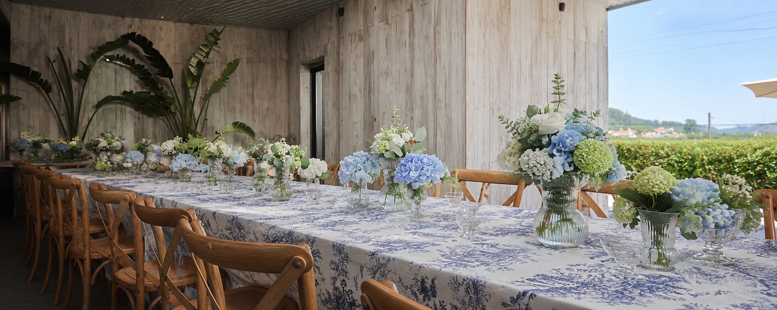 Mesa comprida decorada com hortênsias azuis e verdes, flores brancas e folhagem para evento pela Paula Florista