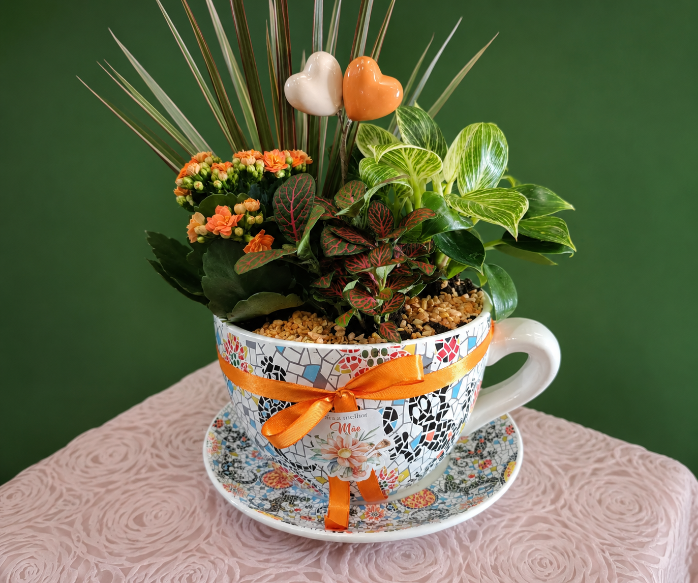 Composição de plantas verdes e flores laranja numa chávena decorativa preparada pela Paula Florista